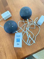 Two Echo Dot units with attached white power cords and adapters on tabletop