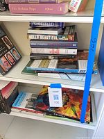 Three shelves showing stacks of assorted books including German, Hello Beautiful, Mike Pompeo, Sacred Duty and Chihuly