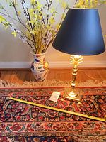 Lamp, vase with artificial forsythia on rug, tape measure showing size