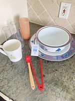Group of all items on countertop—plate, bowl, mug, scraper, tongs, cups