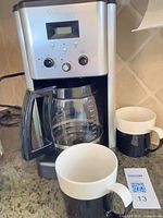 Coffee maker with glass carafe and two mugs on countertop