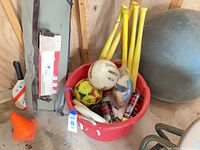 Sports equipment in red bin: bats, balls, paddles, cone, exercise ball