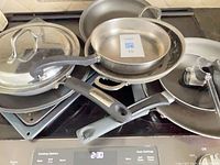 Stacked cookware showing variety of frying pans, lids and broiler tray