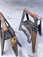 Pair of plastic sawhorses and two hand saws on snow
