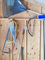 Rake, broom, Great Neck hand saw, bow hacksaw, axe handle visible on shed wall