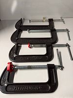 Four black Pittsburgh C-clamps aligned on surface showing overall condition.