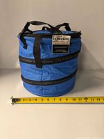 Front view of blue cylindrical cooler bag with tag and measuring tape for scale