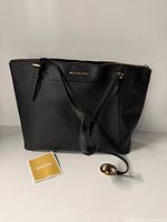 Front view of black Michael Kors tote with charm and booklet