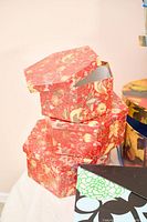 Stack of three red floral hexagonal boxes beside round collage box