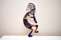 Full view of multicolor metal Kokopelli sculpture standing on base edge