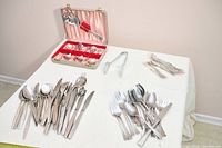 Entire lot laid out on table showing all flatware piles, boxed set, serving tongs