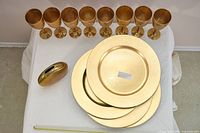 Eight brass goblets, four brass charger plates, brass bud vase displayed on table