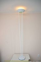 Full view of white metal torchiere floor lamp standing on table
