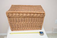Front view of rectangular wicker trunk with lid closed, tape measure showing scale