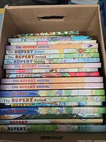 Stack of Rupert Annual hardcover books in box showing spines