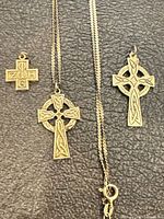 Three gold cross pendants and gold chain laid out on surface