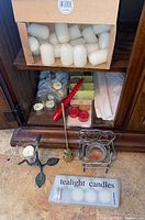 Full view of cabinet shelf showing pillar candles, tealights, candle holders, red spiral candle and pineapple snuffer