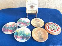 Group shot showing square wine label coaster upright in holder, five round floral coasters and additional floral coaster stack