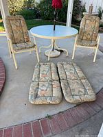 Round white metal patio table with two chairs and cushions placed on ground