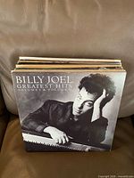 Front cover of Billy Joel Greatest Hits Vol. I & II with rest of stacked albums behind