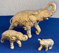 Three ceramic elephant figurines with weeping gold finish displayed on blue surface