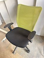Full view of chair showing green mesh back, black seat, armrests, wheeled base