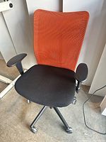 Front view showing orange mesh back, black seat, armrests, 5-leg caster base