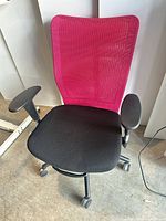 Front view showing pink mesh backrest, black seat, arms and casters