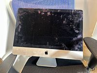 Front view of Apple iMac showing glass display, aluminum bezel, Apple logo, visible smudges