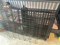 Folded black metal wire panels of large and small dog crates leaning against shelving