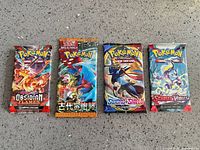 Four sample sealed Pokémon booster packs laid out: Obsidian Flames, Japanese pack, Sword & Shield, Scarlet & Violet