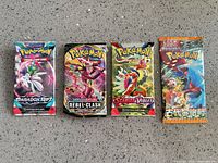 Four sealed Pokémon booster packs laid out side-by-side