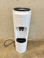 Full front view of white freestanding water cooler with power cord