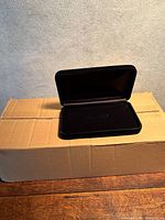 Closed black velvet jewelry box resting on cardboard carton