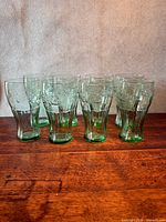 Eight green Coca-Cola embossed glasses arranged upright on wooden surface
