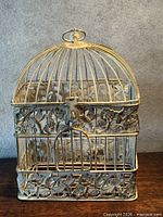 Front view of decorative metal bird cage showing filigree panels and hinged door