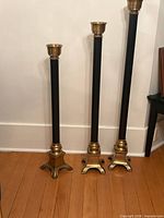 Three floor-standing brass and black candlesticks side by side