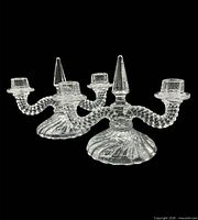 Front view of both Fostoria crystal double candle holders showing arms, cups, and finials