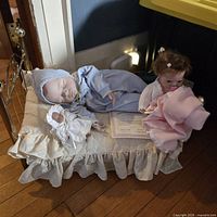 Overall view of two porcelain baby dolls, small cloth doll, certificate and ruffled doll bed