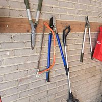 Four garden tools hanging: hedge shears, bow saw, lopper, string trimmer