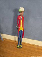 Full view of tall painted wood statue against wall