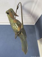 Front view of brass and copper parrot sculpture hanging from swing