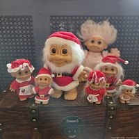 Group shot of seven Christmas-themed troll dolls on wooden chest