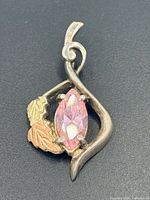 Front view of pendant showing silver frame, gold leaves, pink marquise stone