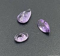 Three loose faceted amethysts on dark surface