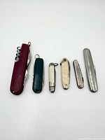 Front view of six pocket knives aligned showing handles