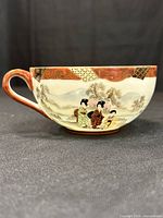 Side view of Satsuma eggshell porcelain tea cup showing hand-painted figures and landscape