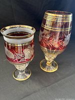 Front view of both glass urns showing size difference and decorative motifs