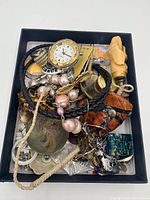 Top view of full box of mixed jewelry items including watch, pearls, pendants