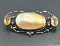 front view of brooch showing mother of pearl center and yellow stones
